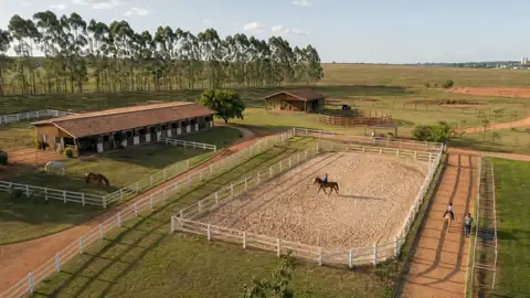 Vista aérea de um núcleo equestre com picadeiro, baias e cercas brancas em área rural